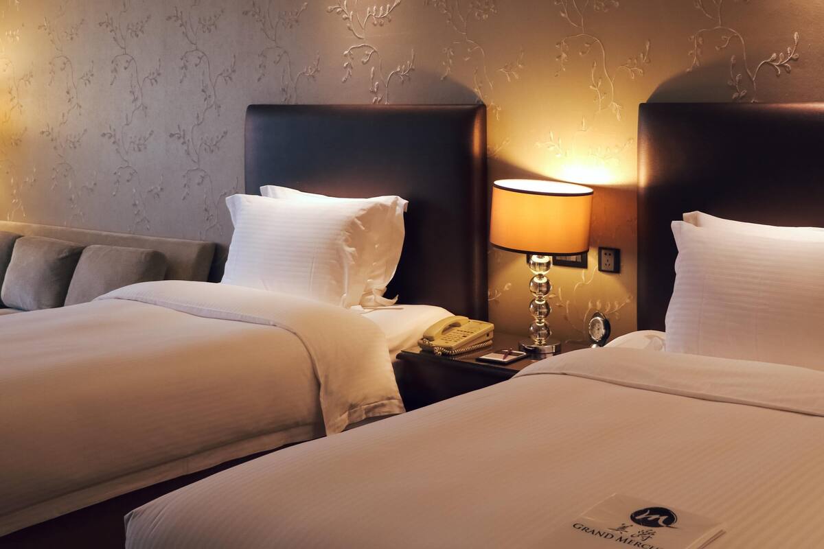 Een hotelkamer met twee bedden, een nachtkastje met een lamp, een telefoon en een wekker.