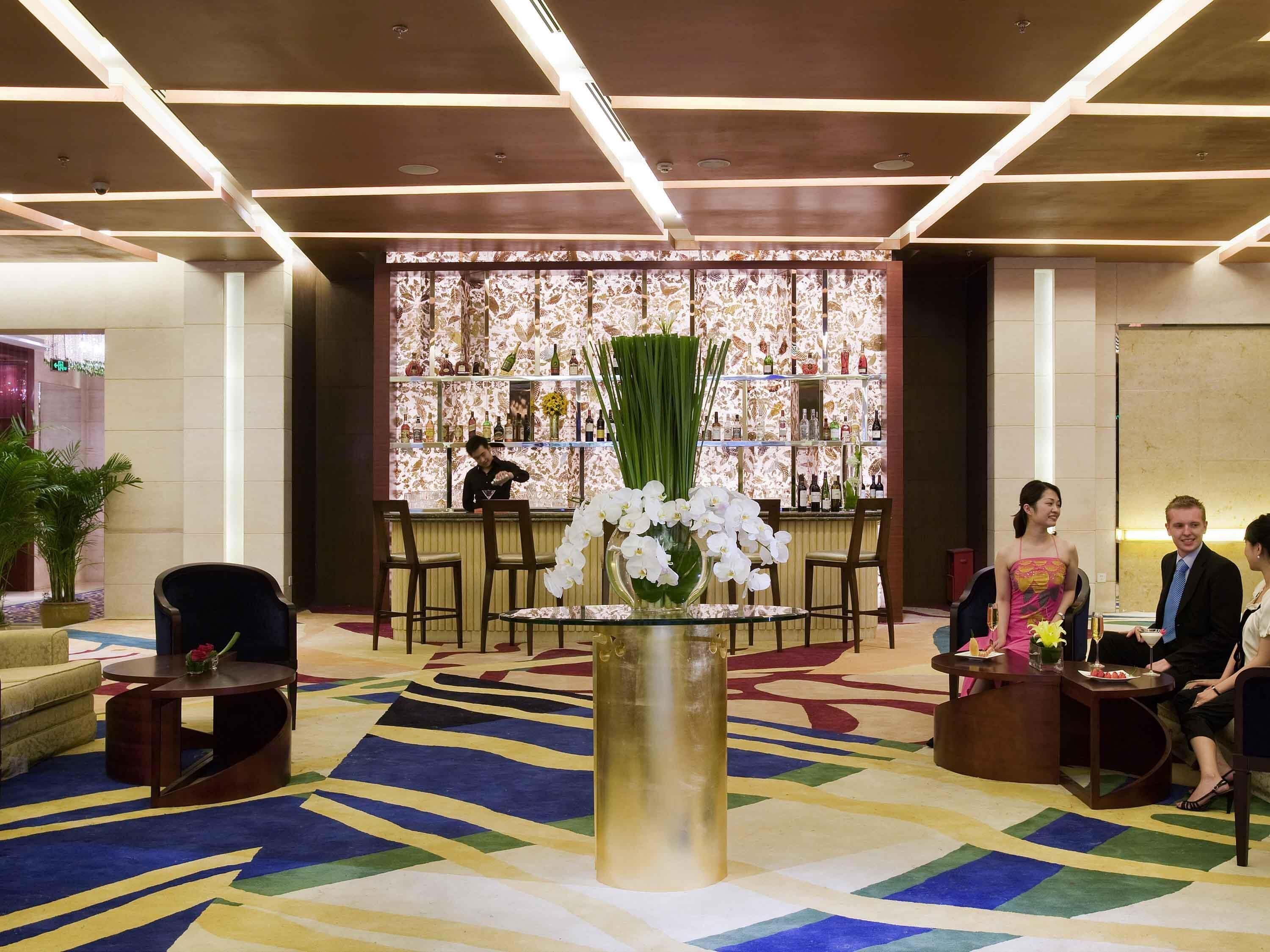 Un hall con zona de bar, diferentes disposiciones de asientos y alfombra estampada.
