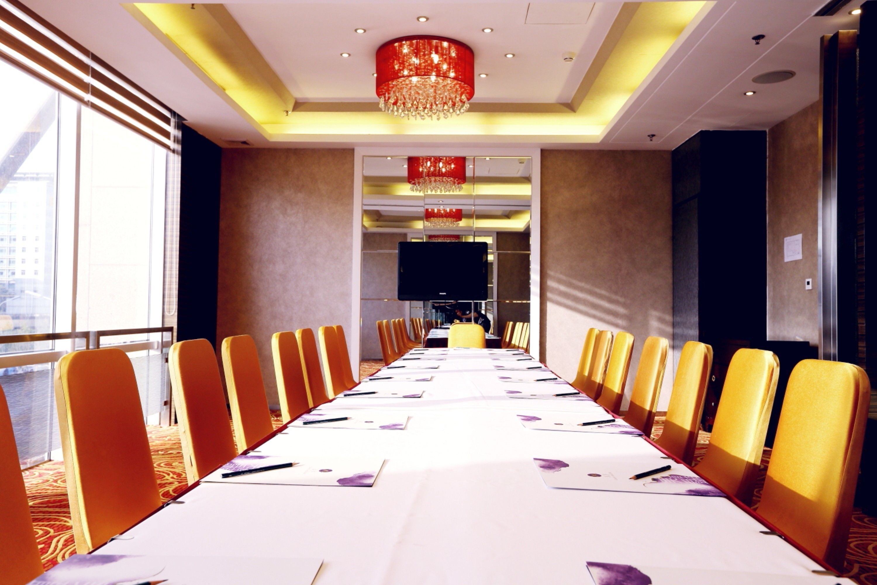 A conference room with a long table, yellow chairs, and a chandelier.