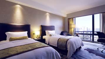 Une chambre d’hôtel avec deux lits, une grande fenêtre donnant sur la ville, un bureau avec une lampe et une chaise.