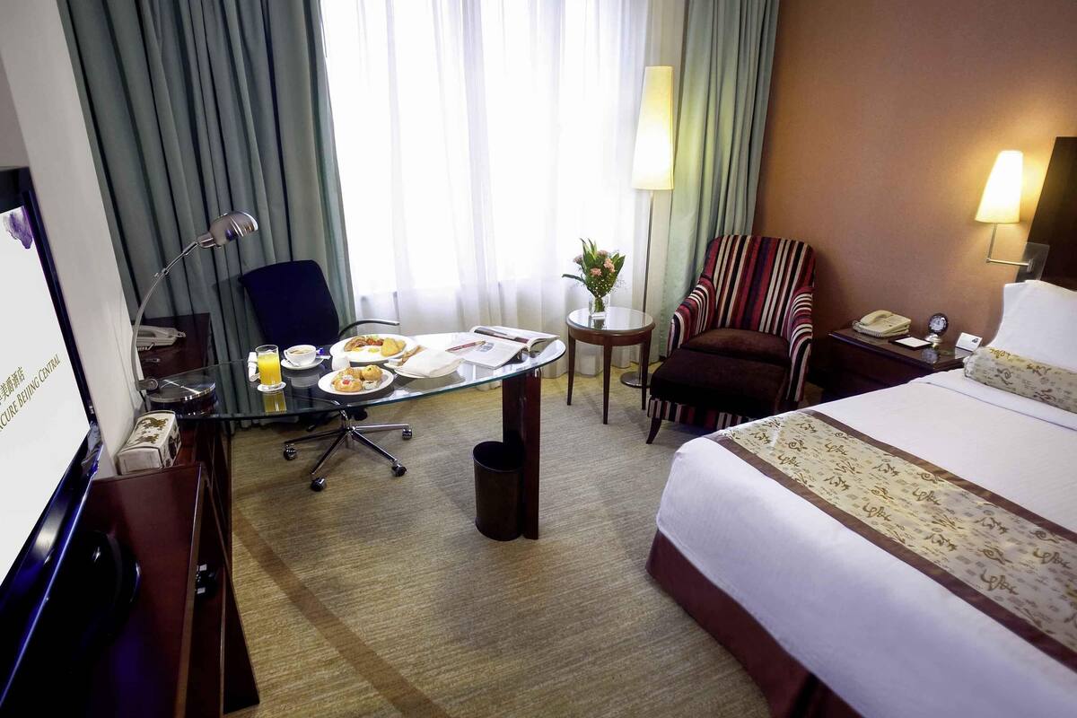 Hotelkamer met een bed, bureau met ontbijt, stoel, lamp en uitzicht op het groen.