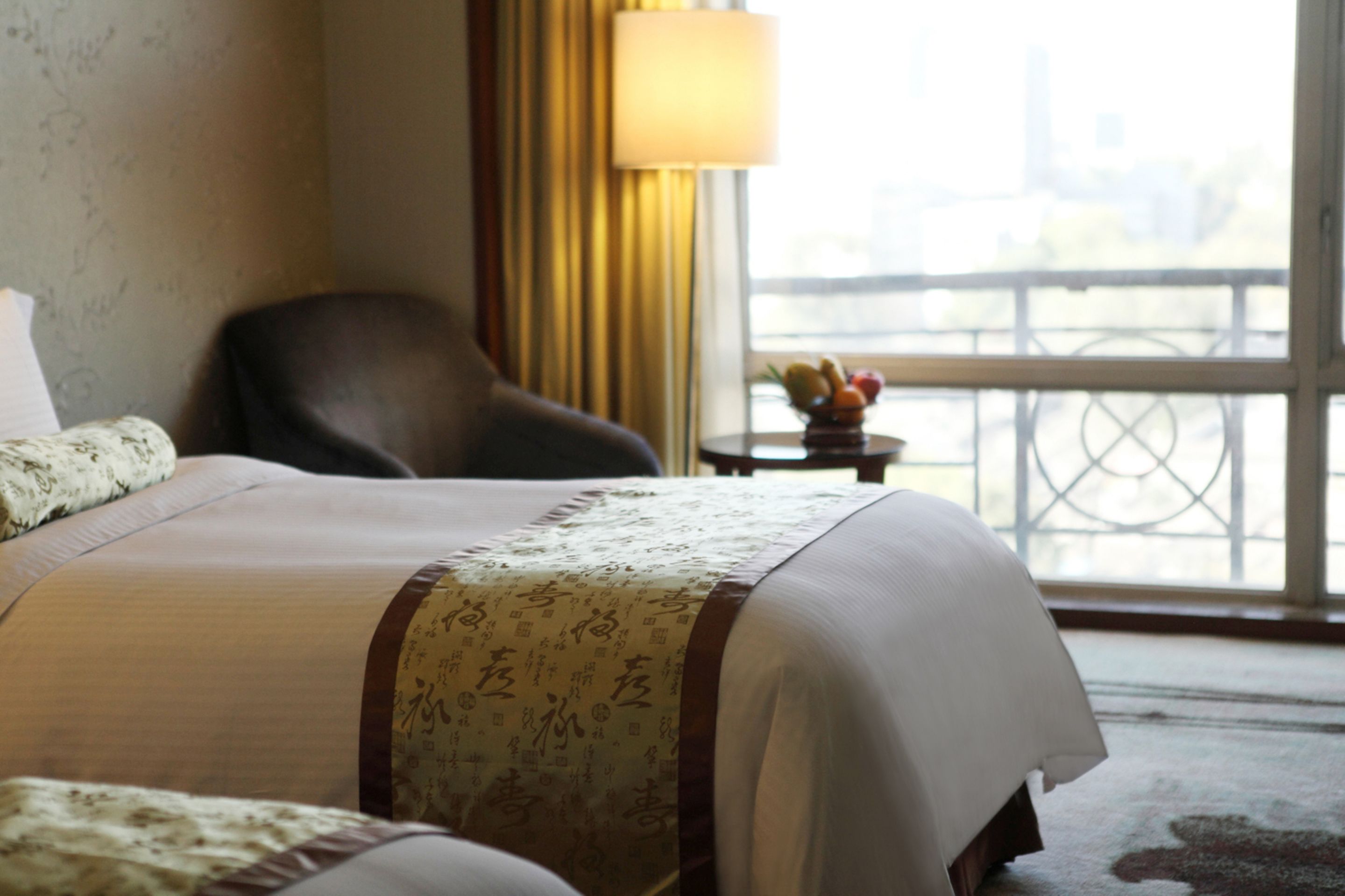 A hotel room with a bed, a chair, a small table with fruit, and a view of a balcony with a railing.