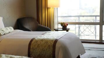 A hotel room with a bed, a chair, a small table with fruit, and a view of a balcony with a railing.