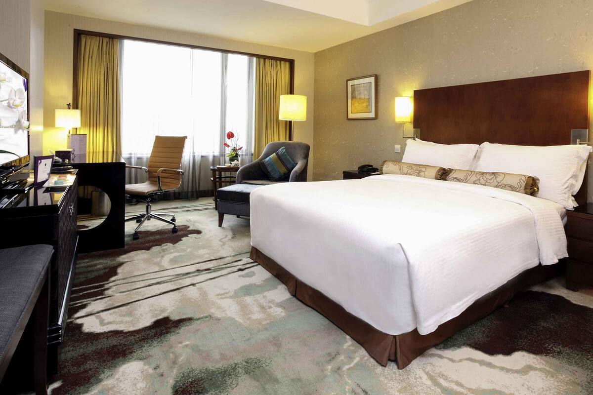 Een hotelkamer met een groot bed, een bureau met een computer, een stoel en uitzicht op het buitengebied.