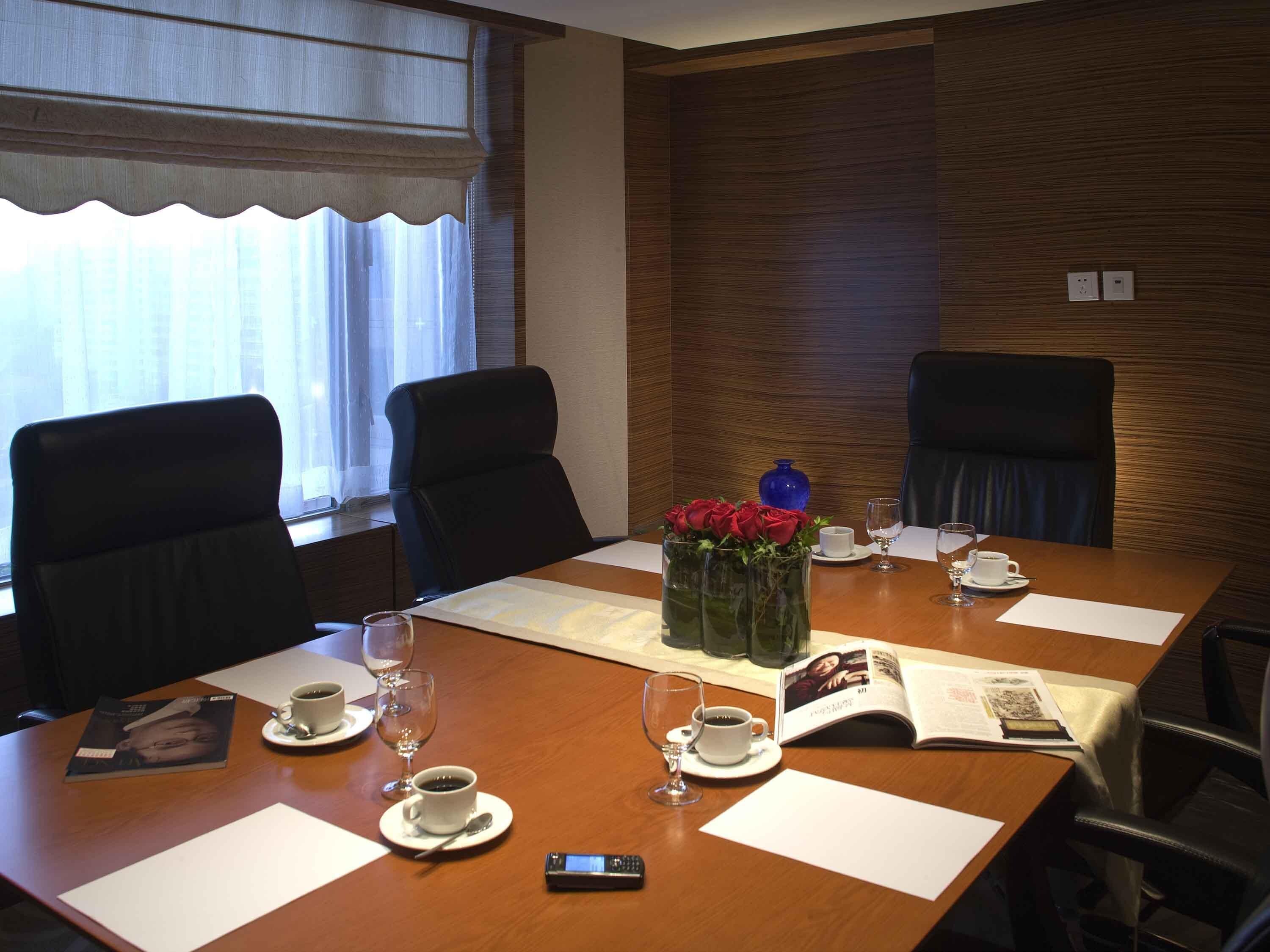 A conference room with a wooden table, two chairs, a vase with red flowers, and a magazine.