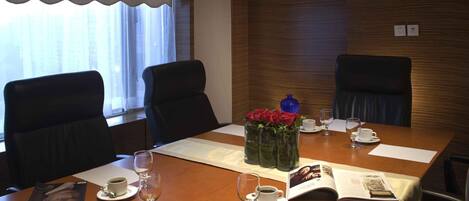 A conference room with a wooden table, two chairs, a vase with red flowers, and a magazine.