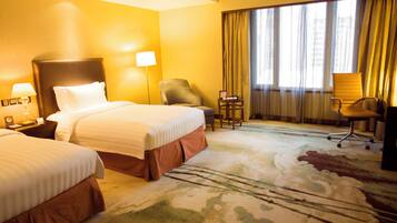A hotel room with two beds, a desk, a chair, and a large window with curtains.