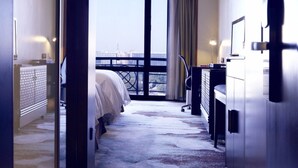 Moderni hotellihuone, jossa on suuri sänky, työpöytä, tuoli ja suuret ikkunat, joista avautuu näkymä kaupunkiin.