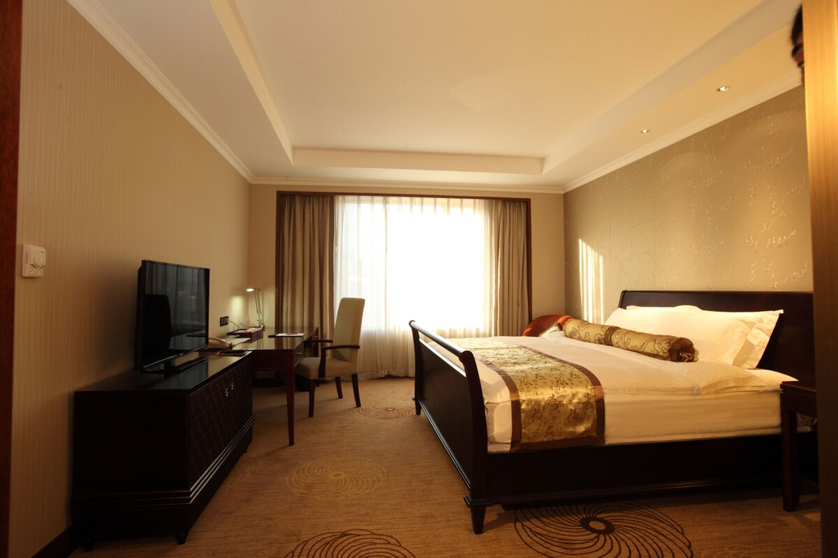 Una habitación de hotel con cama, escritorio con televisor, silla y ventana con cortinas.
