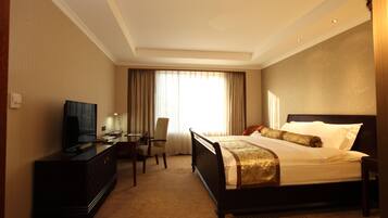 A hotel room with a bed, a desk with a television, a chair, and a window with curtains.