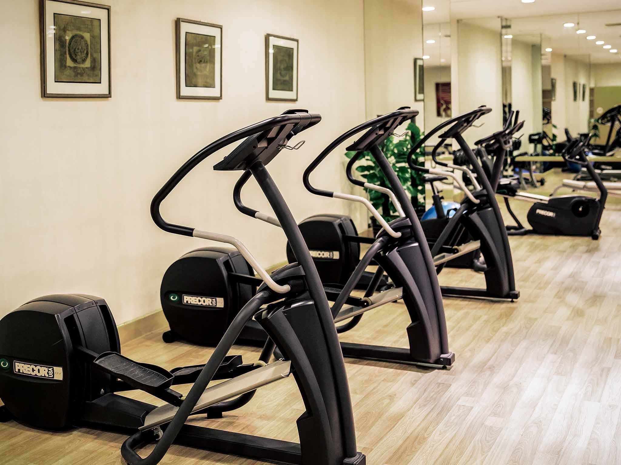 A row of treadmills in a gym with a wooden floor and framed artwork on the wall.