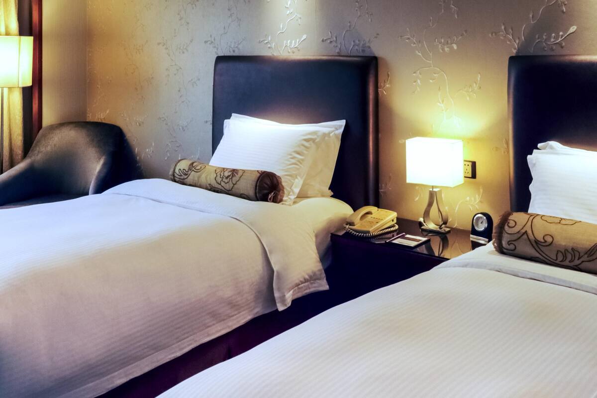 Een hotelkamer met twee bedden, een nachtkastje met een lamp, een telefoon en een klok.