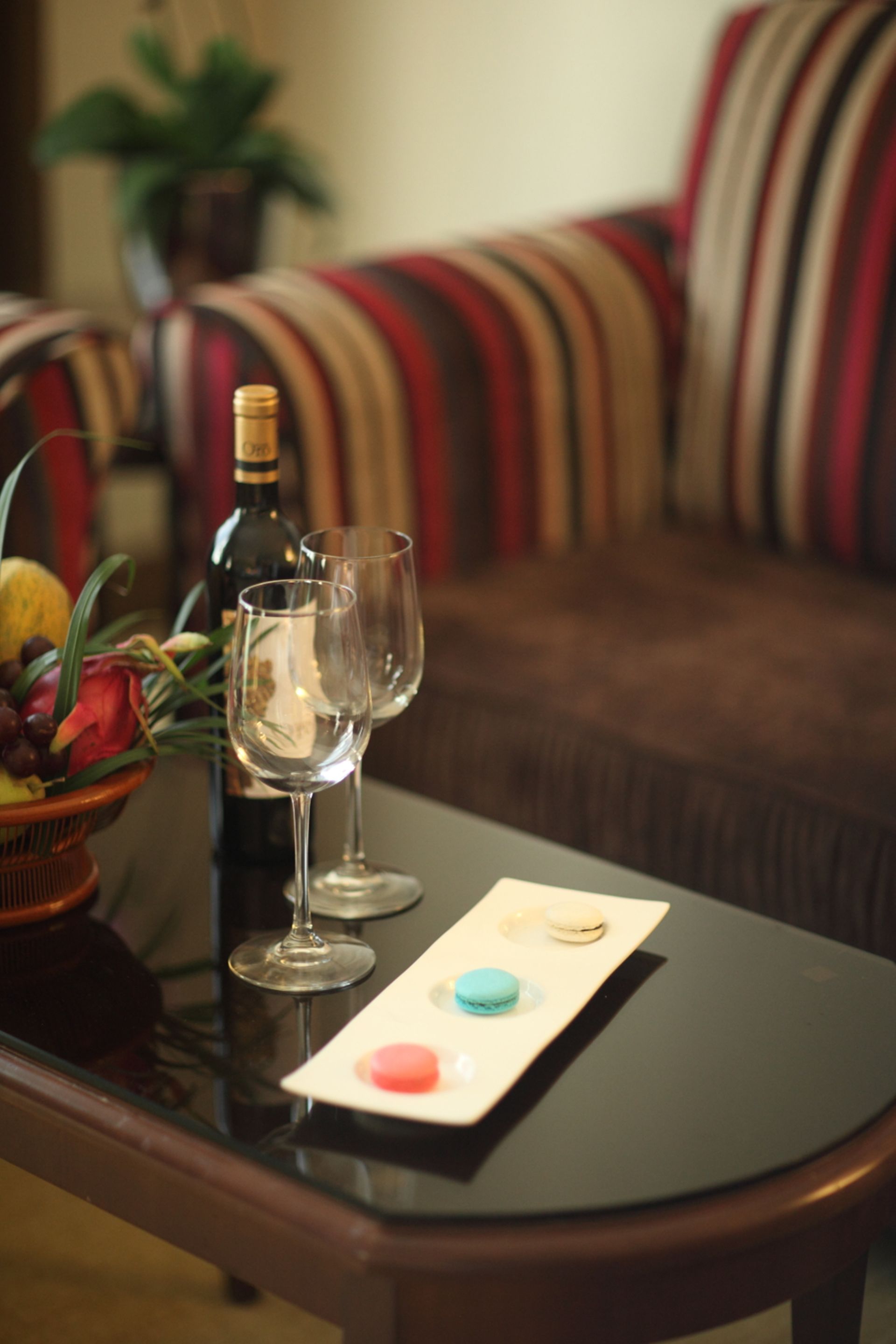 Une table à manger avec deux verres à vin, une bouteille de vin et une assiette de macarons.