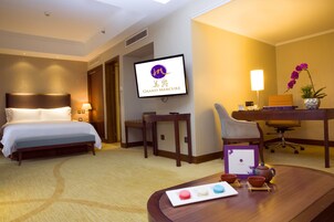 A hotel room with a bed, bedside table, desk, chair, and a TV mounted on the wall.