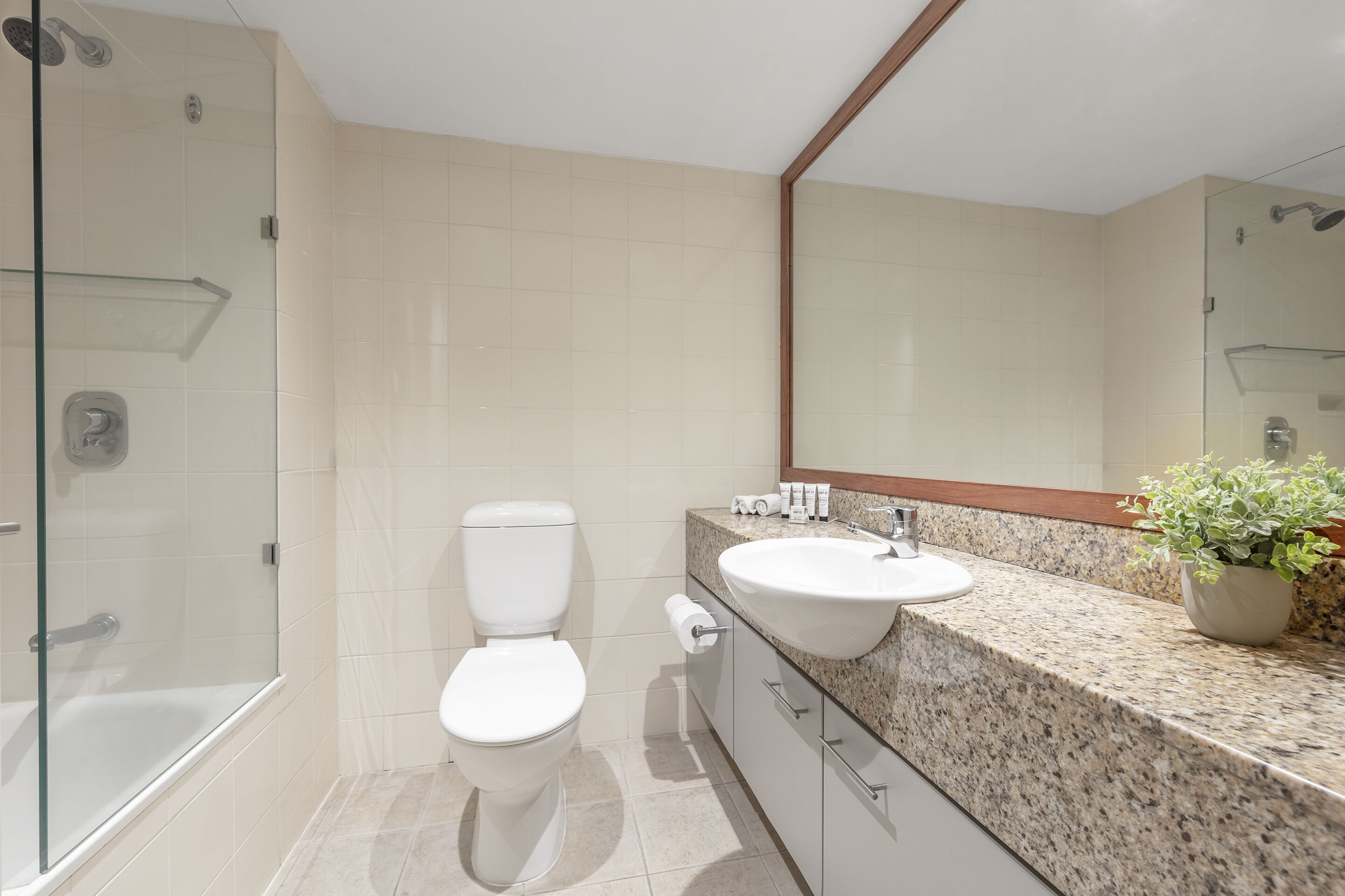 Un baño moderno con cabina de ducha de vidrio, inodoro blanco, encimera de granito con lavabo y espejo sobre el lavabo.