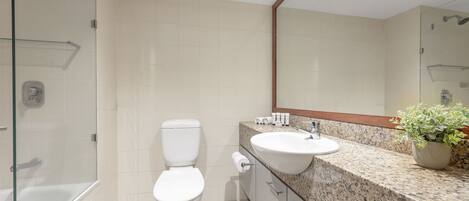 Un baño moderno con cabina de ducha de vidrio, inodoro blanco, encimera de granito con lavabo y espejo sobre el lavabo.