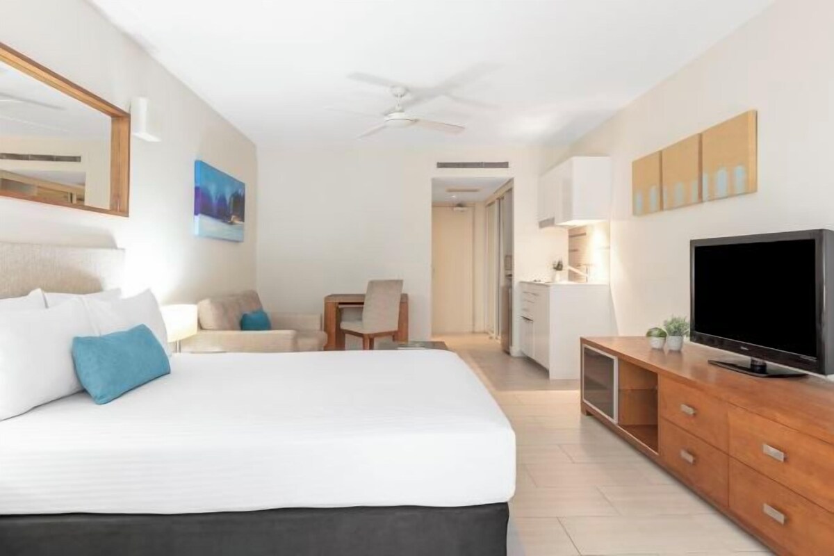A modern hotel room with a large bed, a TV, a desk, and a dining area.