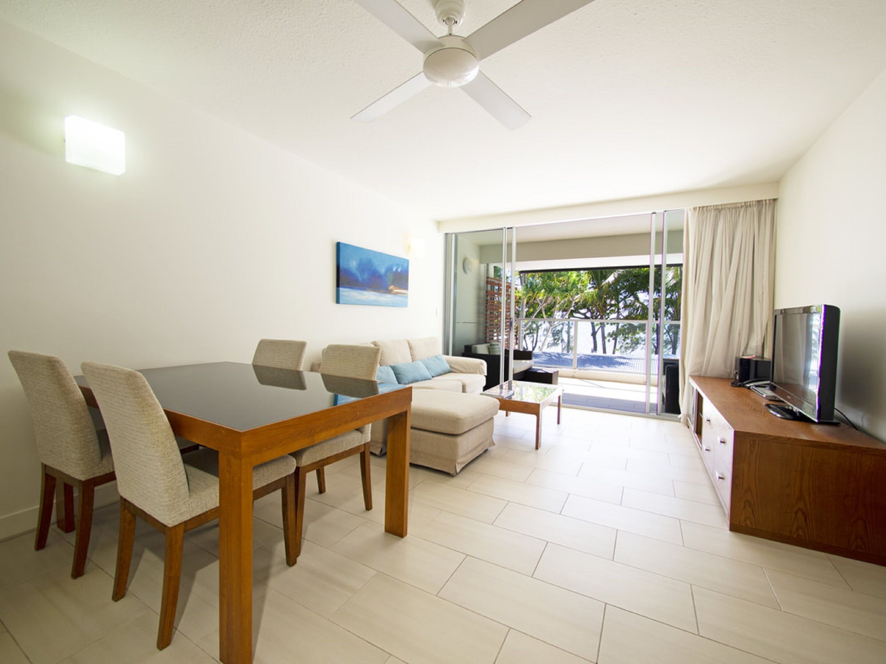 A modern living room with a dining area, a flat-screen TV, and a ceiling fan.