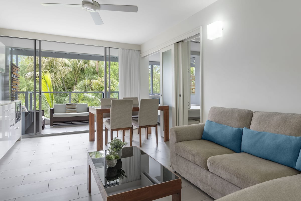 A modern living room with a sofa, a glass coffee table, and a dining area with chairs and a table.
