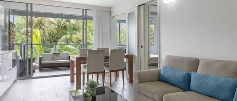 Ein modernes Wohnzimmer mit einem Glastisch, einer blauen Couch mit Kissen und einem Essbereich mit Stühlen und einem Tisch.