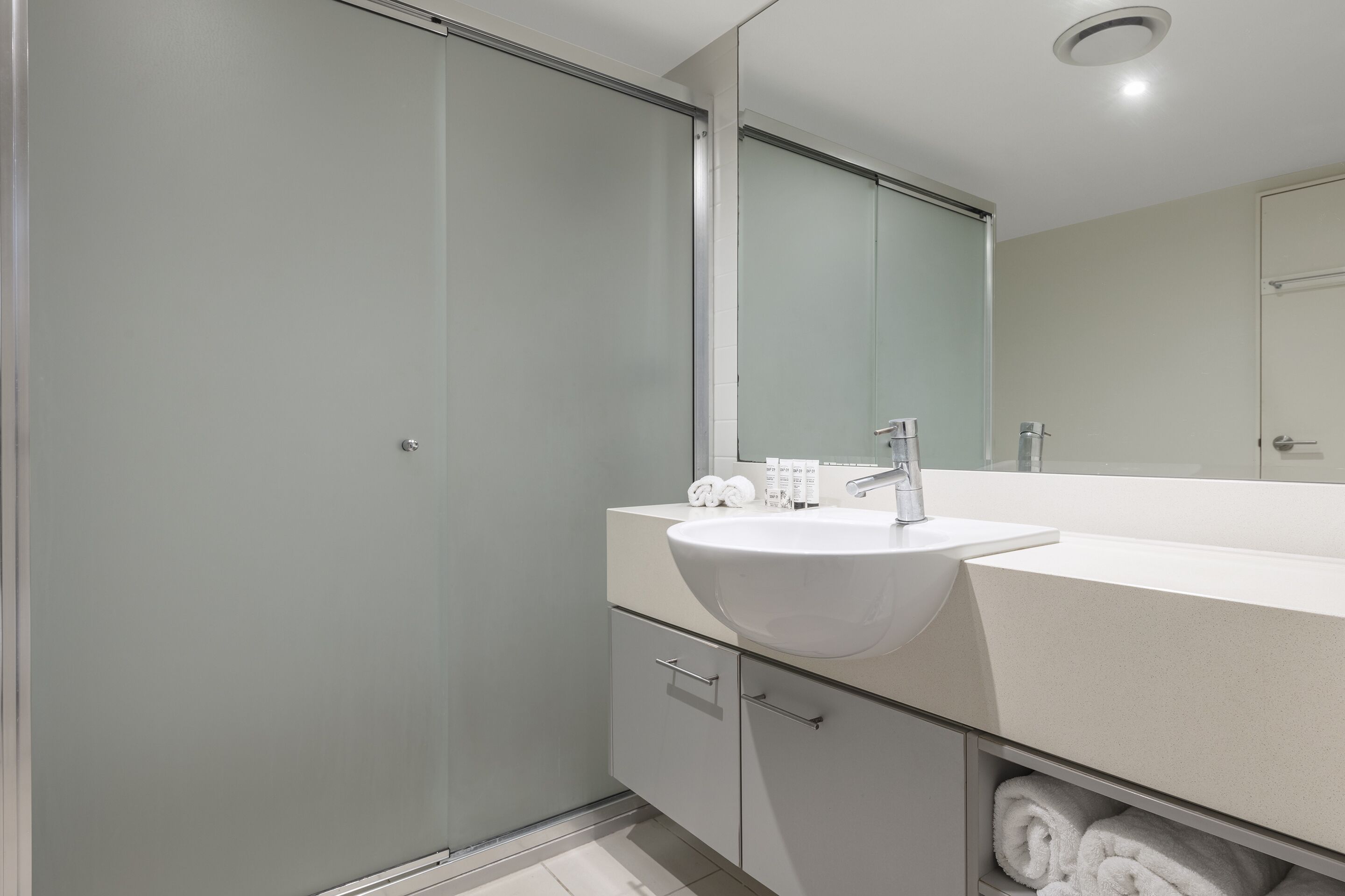 Une salle de bain moderne avec un grand miroir, un lavabo blanc et une cabine de douche en verre.