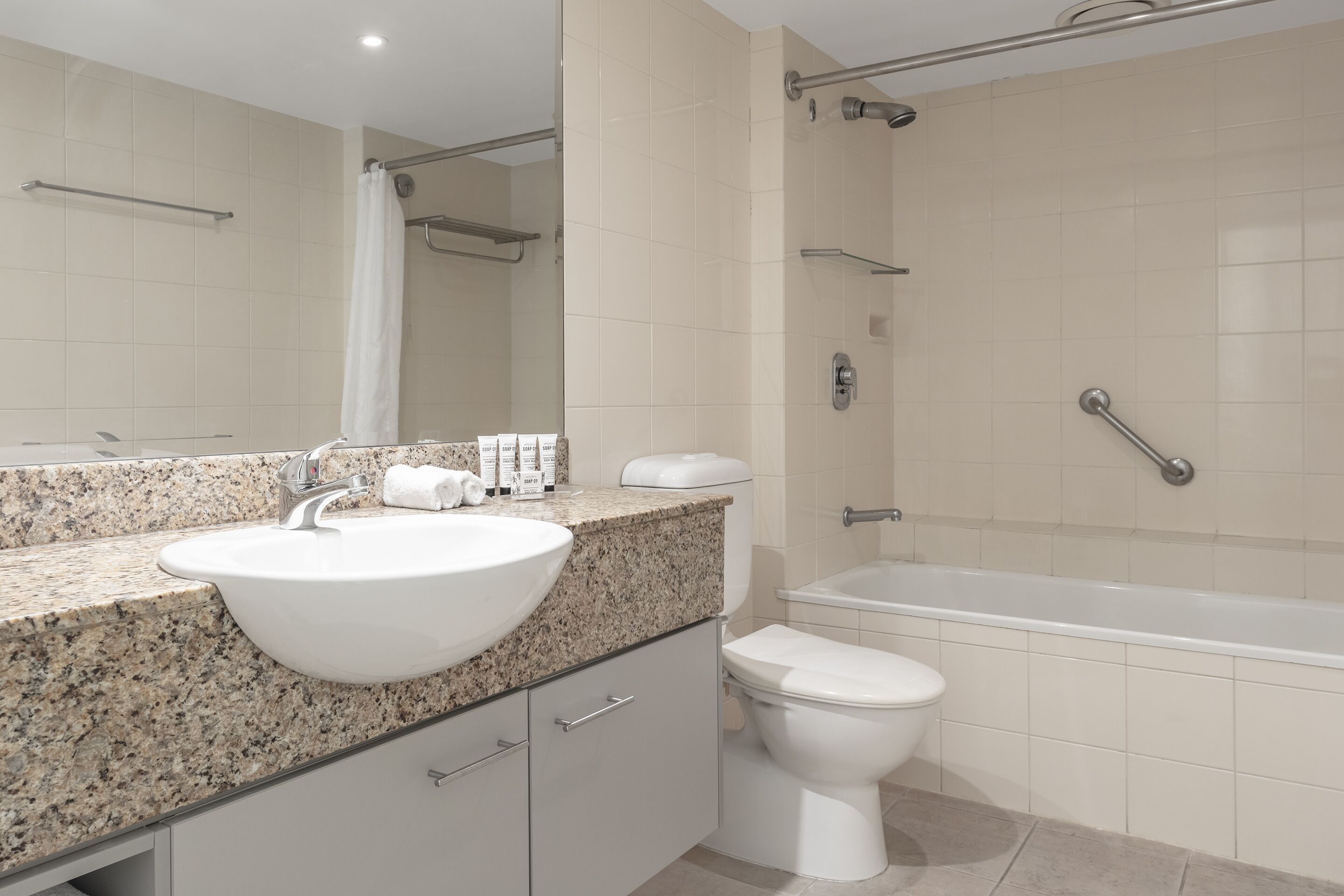A bathroom with a granite countertop, a white sink, a toilet, and a bathtub.