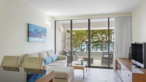 A modern living room with a sofa, coffee table, TV, and a balcony with outdoor furniture. - Drift Palm Cove (Palm Cove)