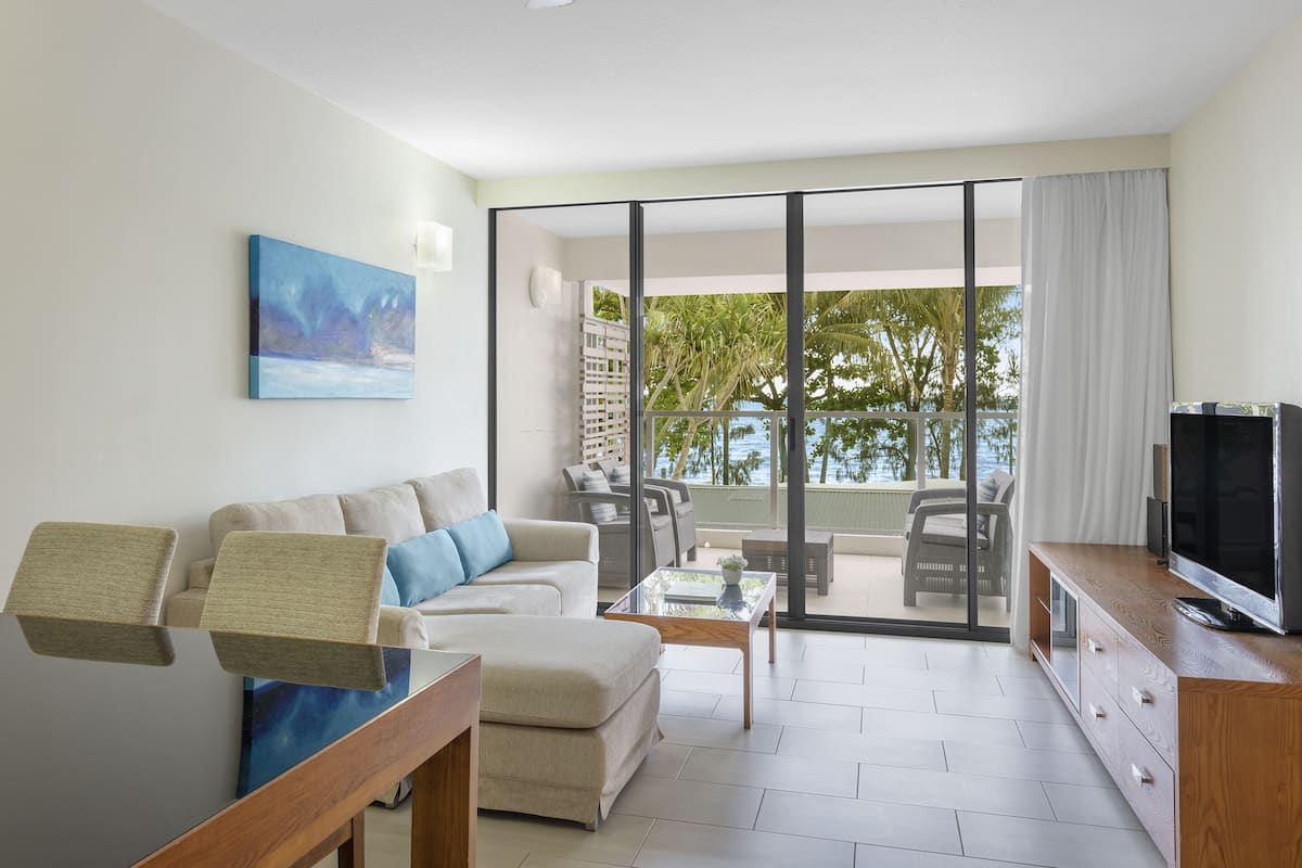 A modern living room with a sofa, coffee table, TV, and a balcony with outdoor furniture.