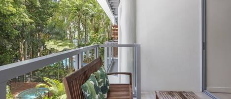 Un balcon avec un banc et une table en bois, donnant sur une piscine et une végétation luxuriante.