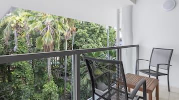 A balcony with a view of dense tropical foliage, a wooden table, and two metal chairs.