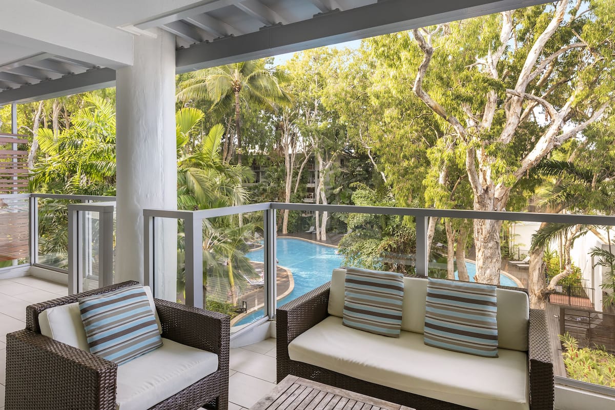 A balcony with wicker furniture and a view of a swimming pool surrounded by trees.