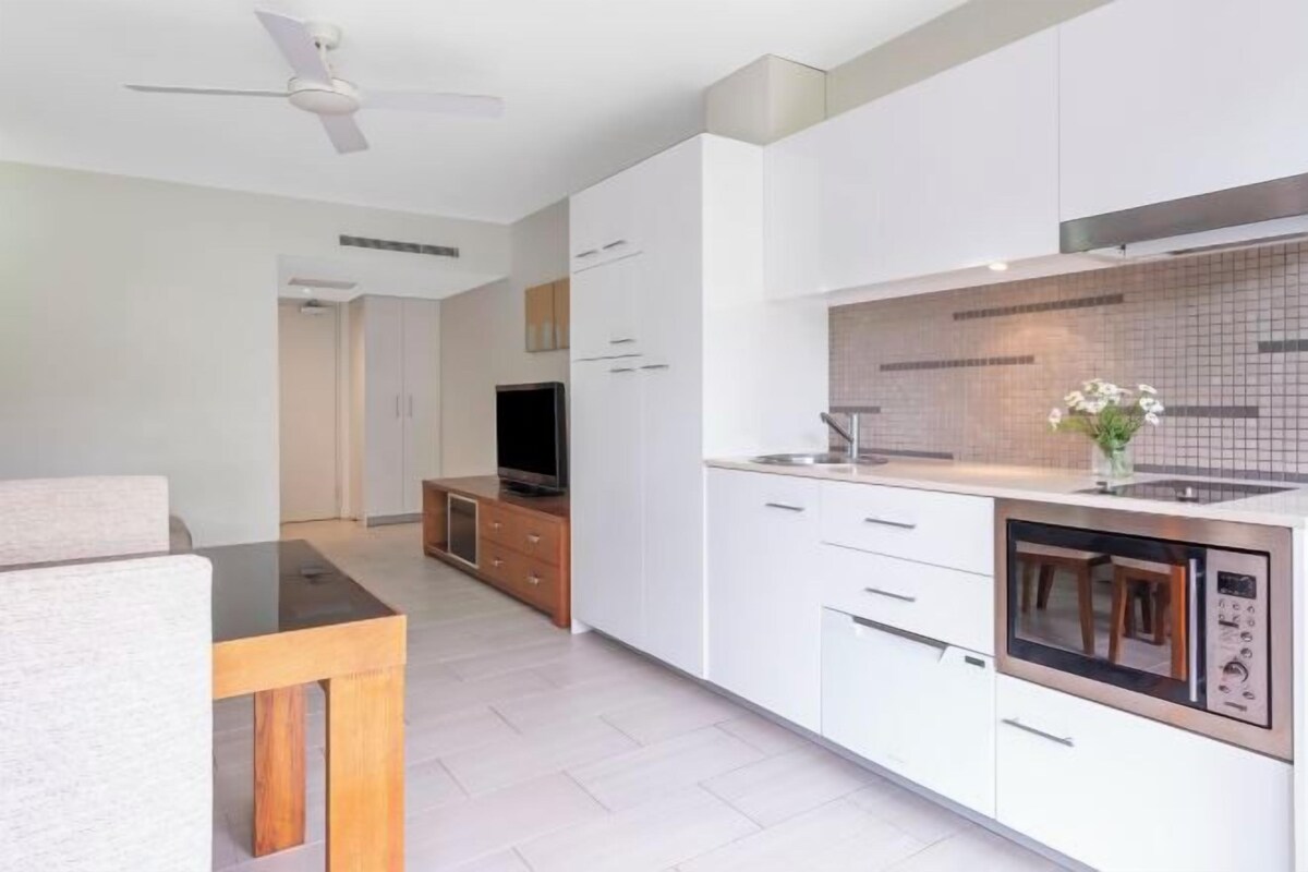 A modern kitchen with white cabinetry, a built-in microwave, and a dining area with a wooden table and chairs.