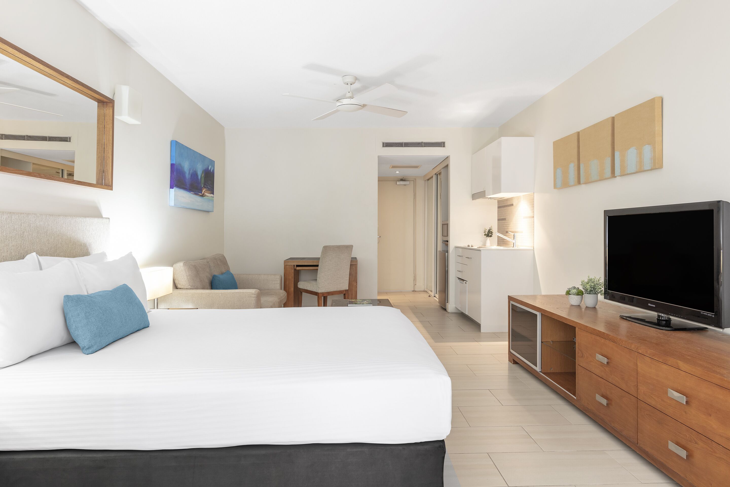 A hotel room with a bed, a desk, a television, and a ceiling fan.