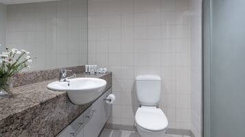 Um banheiro moderno com bancada de granito, pia branca, vaso sanitário e espelho.