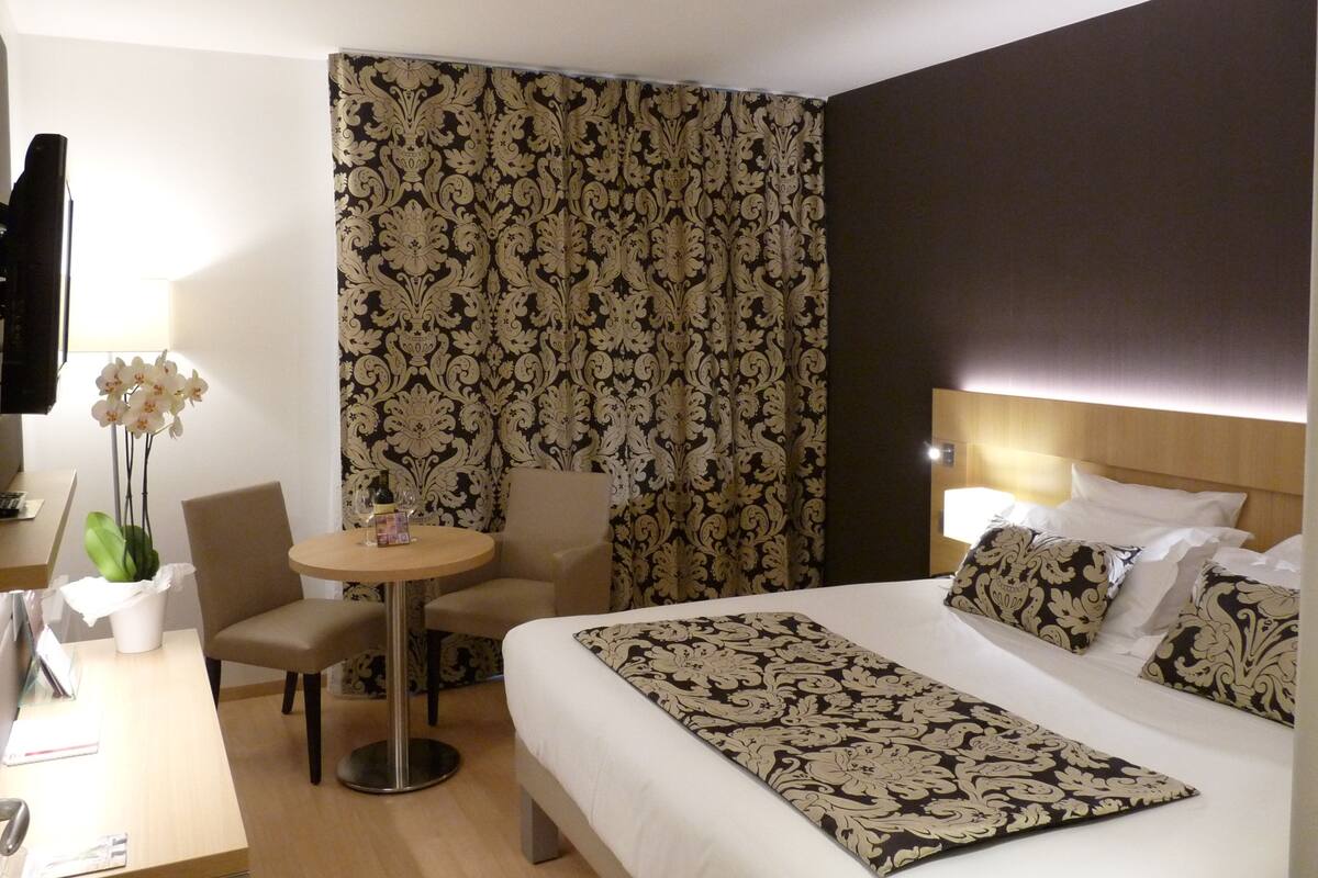 A hotel room with a bed, a desk, a chair, a small table, and a TV.