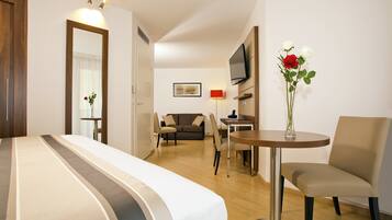 A hotel room with a bed, a TV, a table with a vase of flowers, a sofa, and a chair.