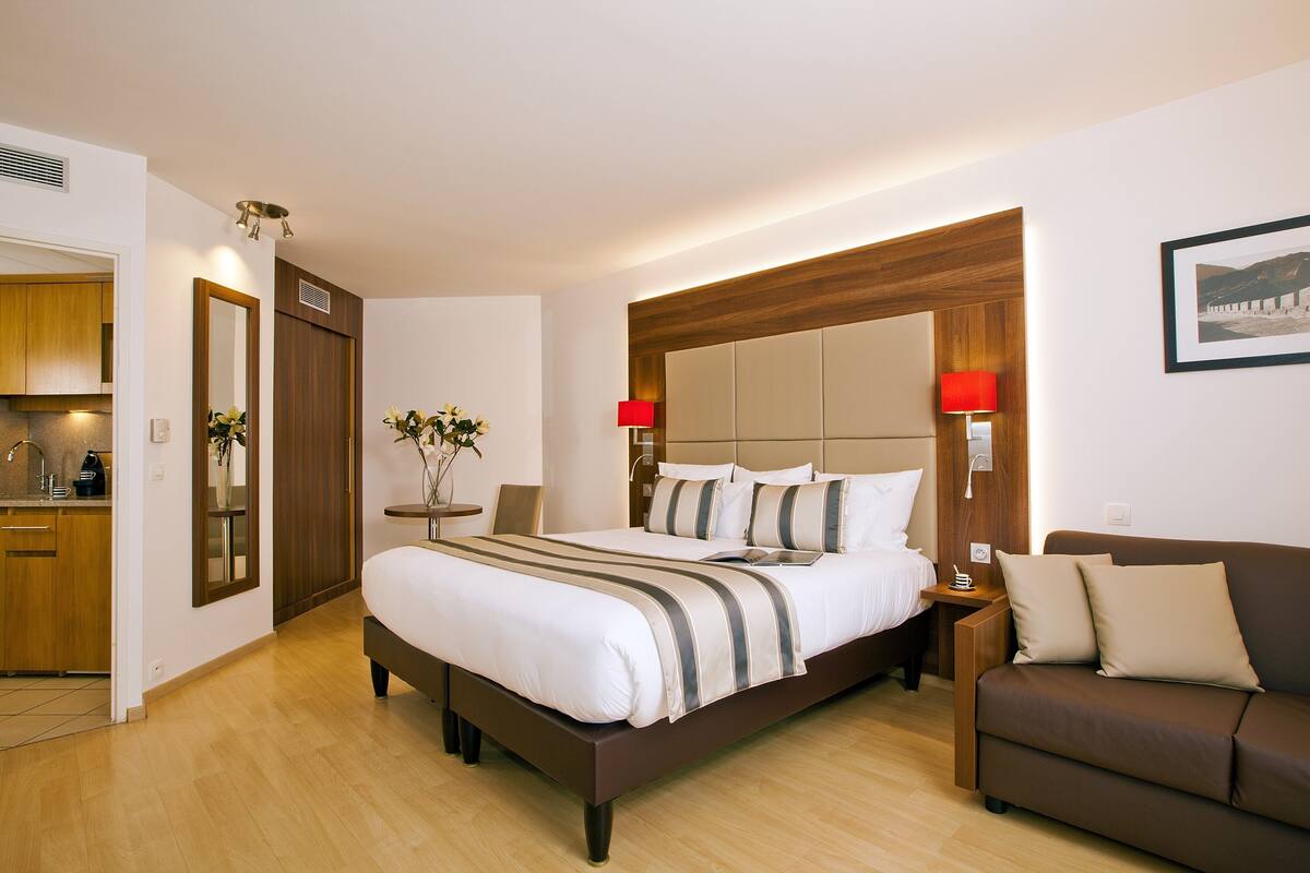 A modern hotel room with a large bed, a sofa, a bedside table, and a small table with a vase.