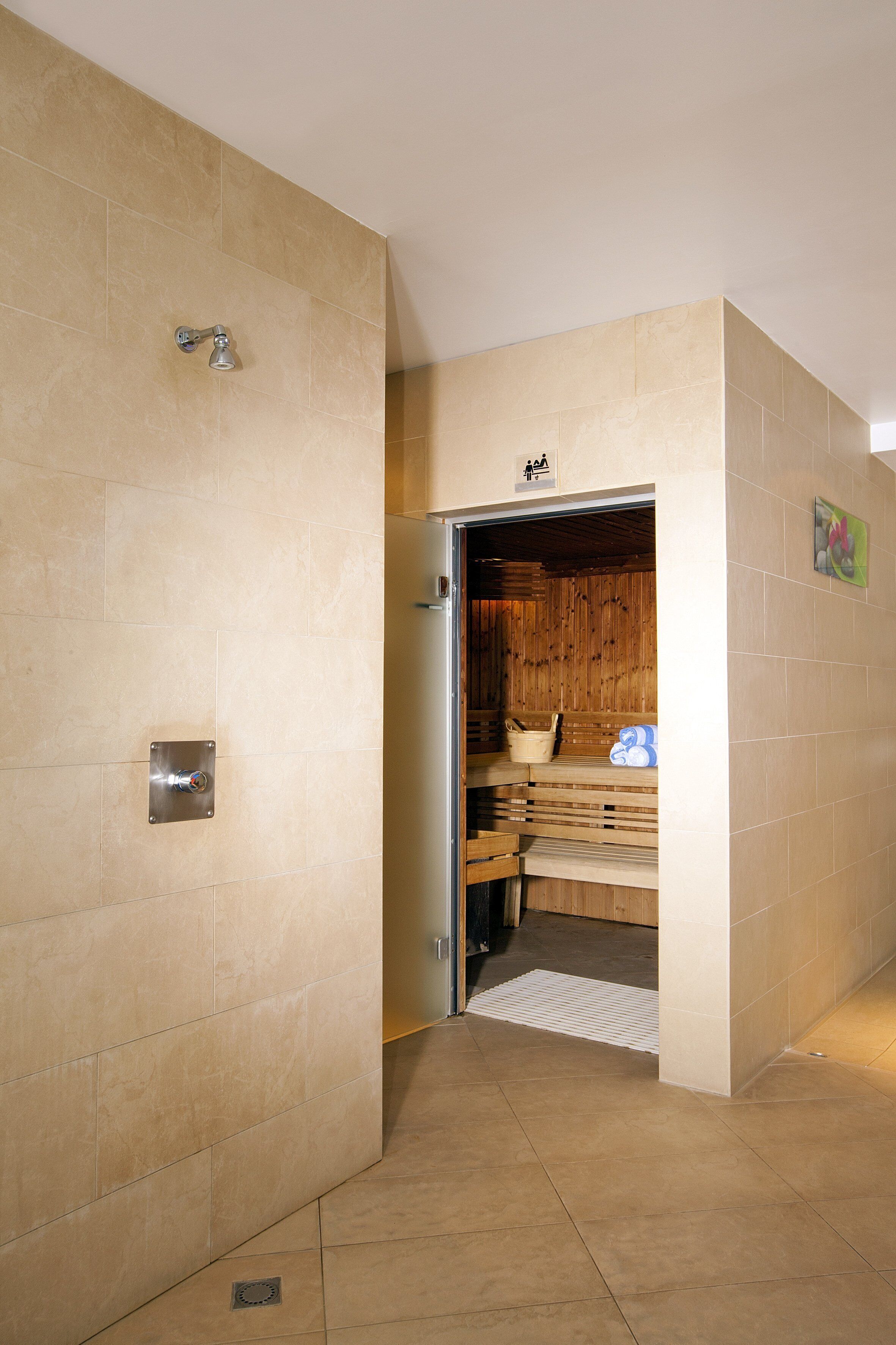 A modern bathroom with beige tiles, a shower, and a wooden sauna area.