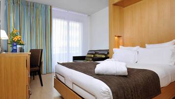 A hotel room with a bed, a desk, a TV, and a window with curtains.