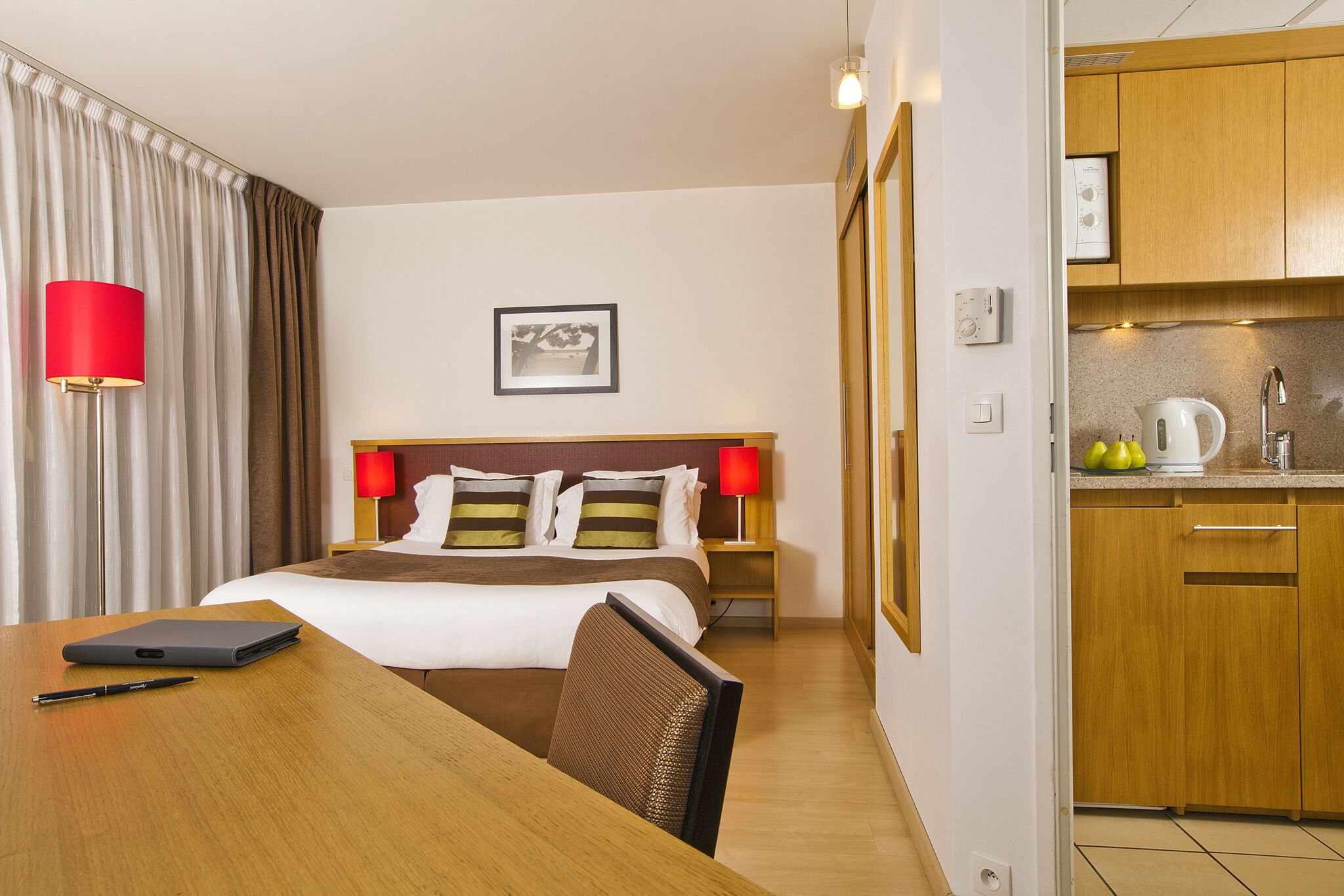 Une chambre d’hôtel équipée d’un lit, de lampes de chevet, d’un bureau avec un ordinateur portable et d’une kitchenette.
