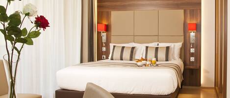 A hotel room with a large bed, bedside lamps, a vase with flowers, and a desk with a laptop.