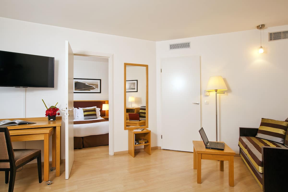 A hotel room with a bed, a desk with a laptop, a TV, a lamp, and a sofa.