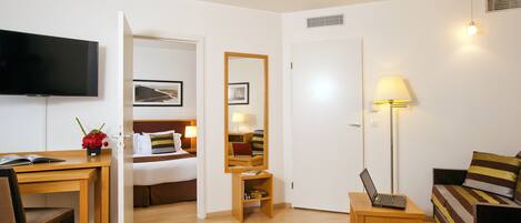 A hotel room with a bed, a desk with a laptop, a TV, a lamp, and a sofa.