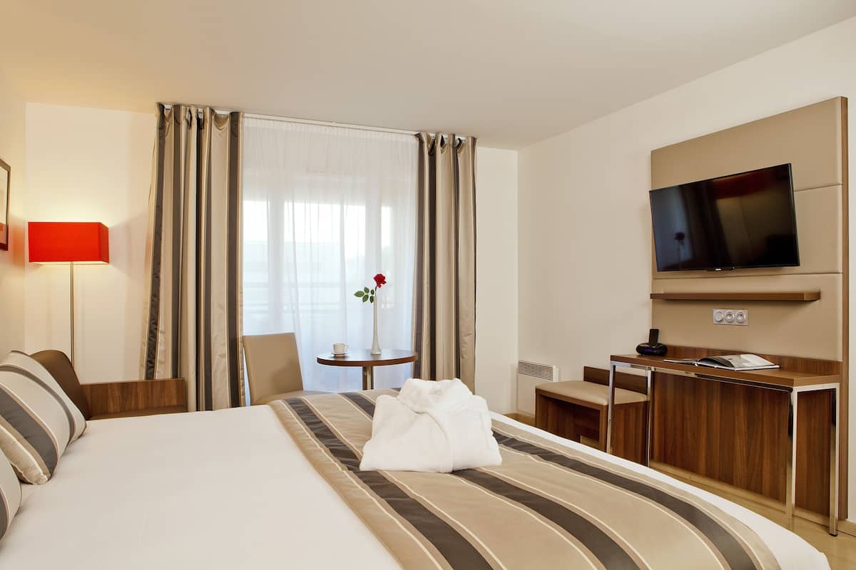 A hotel room with a bed, a desk, a chair, a TV, and a window with curtains.
