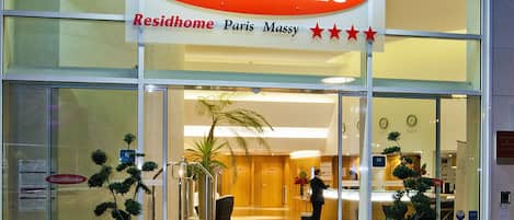 A hotel entrance with a sign reading "Residhome Paris Massy" and a reception desk inside.