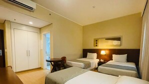 Une chambre d’hôtel avec deux lits simples, un bureau, une chaise et une armoire.