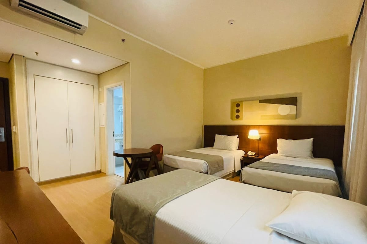 Une chambre d’hôtel avec deux lits simples, un bureau, une chaise et une armoire.