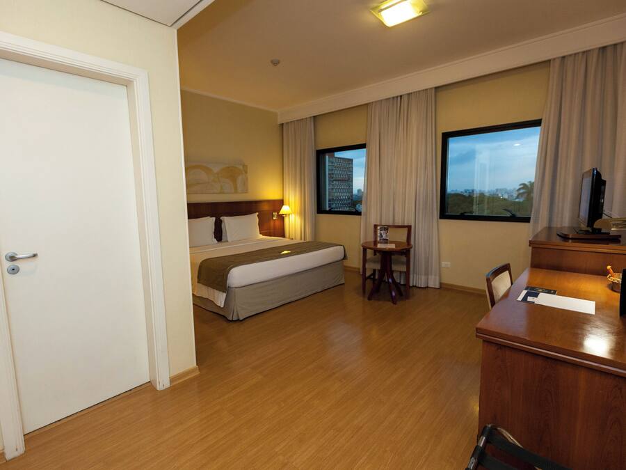 A hotel room with a bed, a desk, a chair, a TV, and a window with curtains.