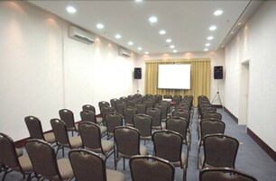 Una sala conferenze con file di sedie, uno schermo per proiezioni e altoparlanti.