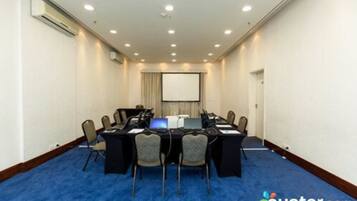 Una sala de conferències amb una taula llarga, cadires, portàtils i una pantalla projectora.
